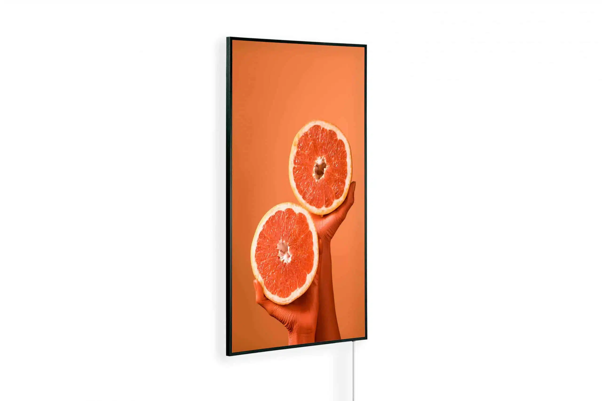 Orange gefaerbte Hand haelt zwei Grapefruithaelften vor orangem Hintergrund